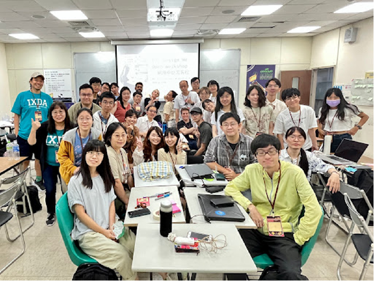 A photo of &ldquo;The Design We Open&rdquo; workshop in Taiwan at COSCUP 2023. There are 20 plus people gathered around a table with laptops, sticky notes and writing on the tables from the workshop. Everyone is looking towards the camera and some people are smiling.