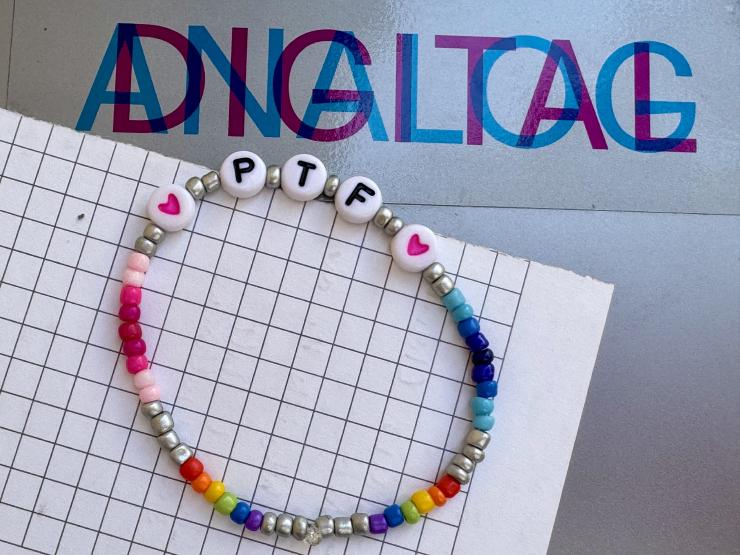 Photograph of a table with a piece of checked paper and a beaded wristband with the initials P T F. Above the wristband is the word ANALOG in blue overlaid by the word DIGITAL in blue.